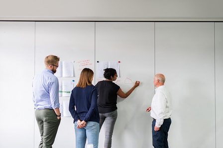 Vier Personen arbeiten gemeinsam an einem Whiteboard